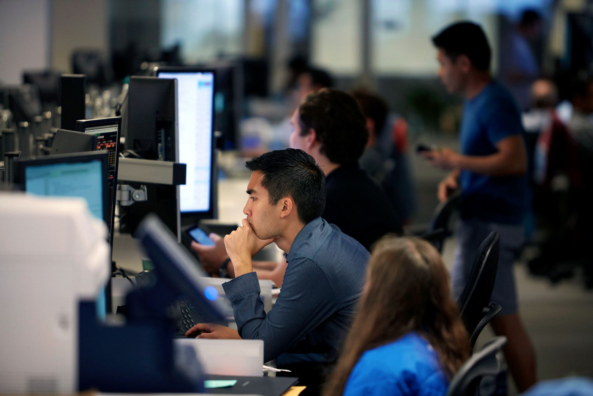 Man sits at his workstation with his chin in his hand, focusing.